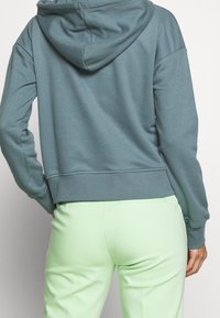 Sudadera con capucha en color verde azulado, fabricada con tela suave, de corte holgado y dobladillo acanalado. Combinada con pantalones de corte entallado en verde claro.