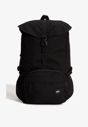 Sac à dos noir Vans avec rabat supérieur, sangle avant à boucle, poche zippée à l'avant et bretelles rembourrées sur fond blanc.