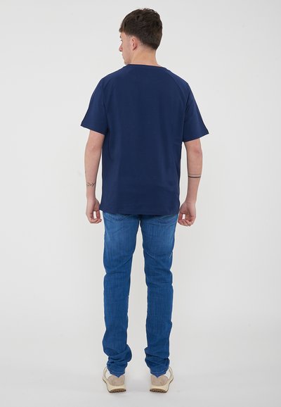 T-shirt blu navy a maniche corte con vestibilità rilassata, abbinato a jeans azzurri. L'outfit presenta un design minimalista senza marchi visibili.