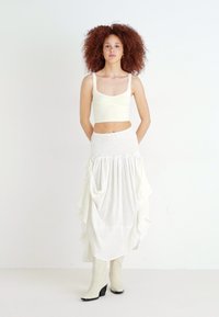White ribbed crop top paired with a flowy, layered white skirt featuring a gathered waist. Model wears knee-high white heeled boots.