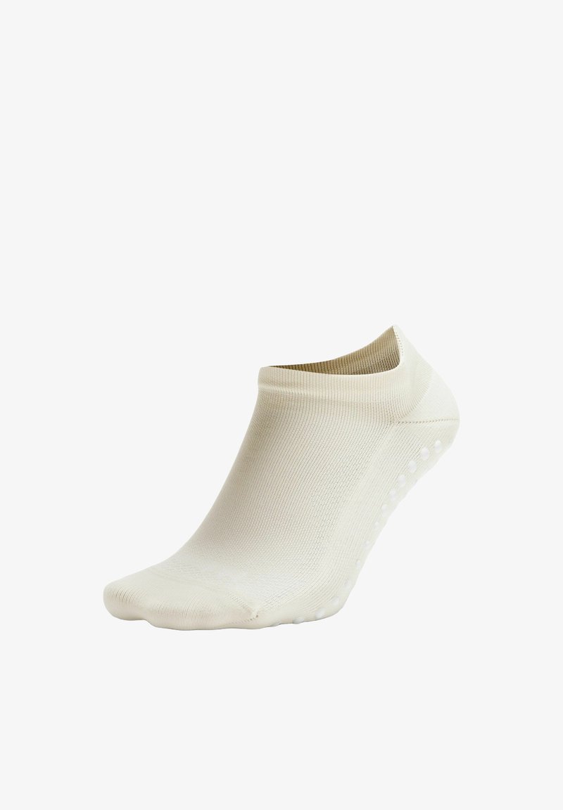 Chaussette beige à coupe basse avec des semelles antidérapantes, fabriquée en tissu lisse et extensible, conçue pour le confort et l'ajustement.