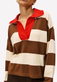 Gestreepte pullover in bruin, crème en rood. Kenmerkt zich door een kraag en een ontspannen pasvorm. Zachte textuur, opvallende verticale strepen en ribgebreide boord.