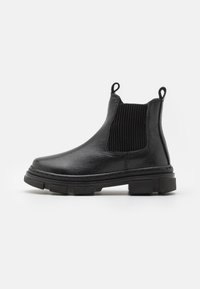 Bota Chelsea de cuero negro con paneles elásticos acanalados a los lados, puntera redonda, bucles para tirar y suela de goma texturizada. Diseño minimalista.