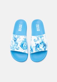 Niebieskie sandały wsuwane z białym paskiem ozdobionym wirującym niebieskim wzorem, wykonane z gładkiego materiału, z teksturowaną podeszwą zapobiegającą poślizgowi.