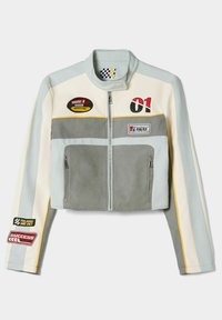 Veste en cuir courte dans des teintes de gris et de blanc, avec une fermeture éclair à l'avant, plusieurs écussons et des accents jaunes. Design texturé et épuré.