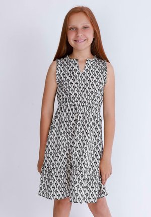 Robe sans manches blanche avec un motif géométrique noir, présentant un décolleté en V et un ourlet à volants en plusieurs niveaux. Tissu léger et tissé.
