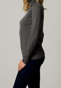 Maglione grigio a collo alto realizzato in morbido tessuto a maglia, con maniche lunghe e un design aderente, abbinato a pantaloni blu scuro.