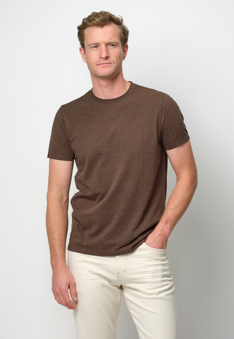 T-shirt marrone a maniche corte in un fit rilassato, realizzato in un tessuto texturizzato, abbinato a jeans chiari. Design semplice con scollatura rotonda.