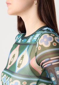 Top in rete trasparente con un design grafico colorato che presenta lanterne, fiori e motivi geometrici, prevalentemente in verde, blu e rosa.