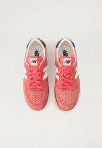 Baskets en daim rouge avec des accents blancs sur les côtés et un bout perforé. Laces roses et talon bleu marine. Semelle extérieure en caoutchouc offrant une bonne adhérence.