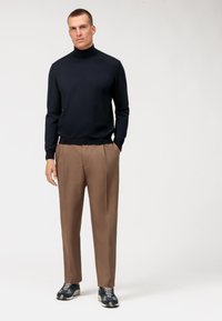 Maglione a collo alto blu navy, pantaloni tailleur marroni e scarpe sportive con motivo. Tessuto liscio, design aderente e tasche nei pantaloni.