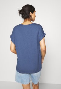 Marineblå bomulls t-skjorte med rullede ermer, rund hals og løs passform, kombinert med lyse denimshorts.