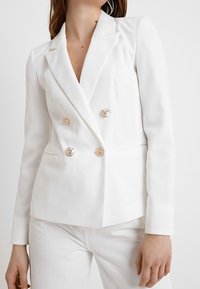 Bílý dvouřadý blejzr s klopami, zdobený zlatými knoflíky a přiléhavým střihem. Hladká textura, minimalistický design.