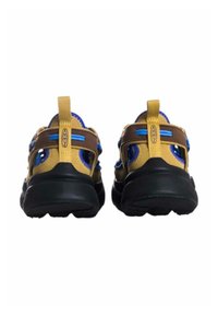 Zapatillas marrones y amarillas con acentos azules, que presentan cortes de malla, una suela negra texturizada y una lengüeta en la parte trasera para ponerse y quitarse fácilmente.