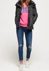 Sort zip-up jakke med lilla accenter over en lyserød sweatshirt, parret med ripped blå skinny jeans og hvide sneakers.