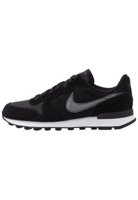 Black athletic shoe featuring a suede and mesh upper, silver Nike swoosh, white midsole, and black rubber outsole with pronounced treads.