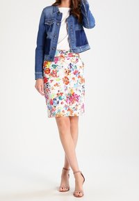 Džínová bunda v modrých tónech, bílá tužková sukně s barevnými květinovými vzory a nahé lodičky na vysokém podpatku.