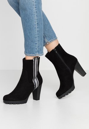 Schwarze Wildleder-Ankle Boots mit einer strukturierten Gummisohle, hohem Absatz und seitlichem Reißverschluss, der mit einem grau-weißen Streifenakzent verziert ist.