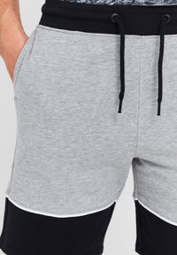 Grå bomulds shorts med sorte accenter, der har en elastisk talje, snøre og sidelommer. Kontraststing fremhæver designet.