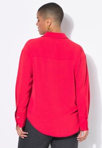 A person with short hair wearing a bright red button-up shirt is seen from behind, displaying the shirt's collar and cuff details.