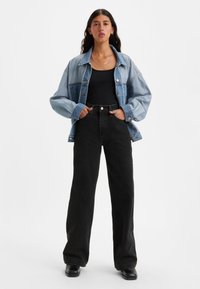 Jakna iz jeansa svetlo modre barve, črna telovnica, hlače z visokim pasom in širokimi nogavicami v črni barvi ter črni čevlji. Jakna ima zapenjanje na gumbe in žepe.