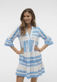 Robe à manches courtes présentant un motif géométrique bleu sur fond blanc, jupe à volants et coupe décontractée avec un décolleté en V.