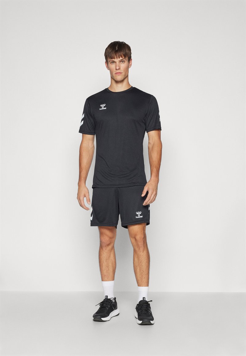 Conjunto deportivo negro que incluye una camiseta de manga corta y pantalones cortos. Ajuste atlético, textura suave, logotipo blanco y detalles blancos en las mangas.