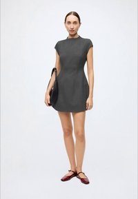 Grå, tætsiddende kjole med kasketærmer, glat tekstur, længde over knæet. Kombineret med en sort taske og vinrøde flade sko.