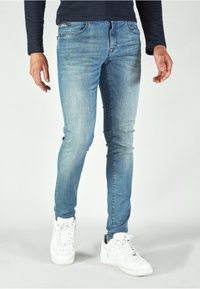 Light blue jeans with a slim fit, featuring a faded wash, traditional 5-pocket design, and worn detailing on the front. Worn with white sneakers.