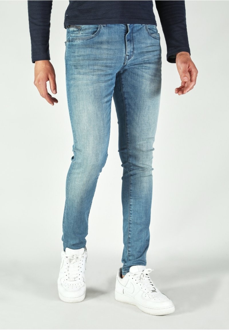 Light blue jeans with a slim fit, featuring a faded wash, traditional 5-pocket design, and worn detailing on the front. Worn with white sneakers.