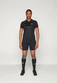 Čierny futbalový dres s krátkym rukávom a červenými akcentmi, zodpovedajúce šortky, čierne ponožky s bielymi pruhmi a čierne futbalové kopačky.