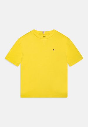 Helles gelbes T-Shirt mit kurzen Ärmeln und Rundhalsausschnitt, mit kleinem rechteckigem rot-weiß-blauem Logo auf der Brust.