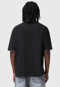 Camiseta negra de manga corta, hecha de algodón, con un corte holgado y un cuello redondo. La parte trasera es lisa y sin adornos visibles.