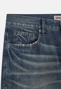 Denim jeans in een vervaagde donkerblauwe kleur, met een versleten rand van de zak, metalen accenten en gestikte details langs de tailleband.