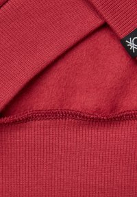 Sudadera de forro polar rojo con un interior suave y dobladillo acanalado. Presenta costuras planas y una etiqueta con un logo en el cuello.