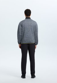 Giacca grigia con texture e colletto nero, indossata con pantaloni neri e calzature nere, vista da dietro su uno sfondo chiaro.