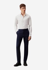 Camicia bianca a maniche lunghe con bottoni, abbinata a pantaloni navy e scarpe eleganti nere, con una vestibilità slim e una texture di tessuto liscia.