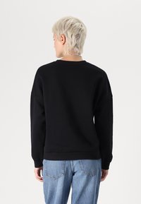 Sudadera negra de corte relajado, con puños y dobladillo acanalados. Material de algodón suave con cuello redondo, combinada con jeans de un azul claro.