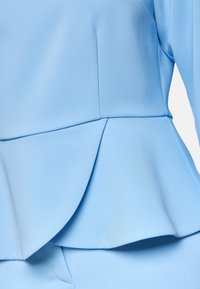 Helles blaues Peplum-Top aus glattem Stoff mit geschichtetem Design. Verfügt über genähte Nähte und einen subtilen Glanz.