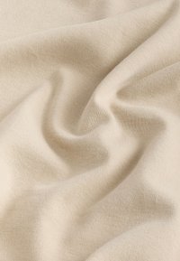 Hellbeiges Gewebe mit glatter Textur, das sanfte Falten und ein feines Strickmuster zeigt. Ideal für Polster- oder Bekleidungsanwendungen.