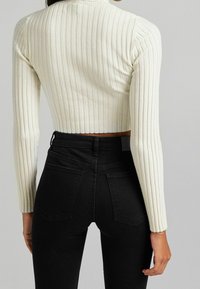 Skuren, ribbad tröja i off-white som är kombinerad med högmidjade svarta jeans. Har långa ärmar och en figurnära silhuett.