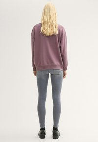 Túlméretes lila pulóver kerek nyakkivágással és bordázott mandzsettával, szürke, slim-fit farmerrel és fekete platform cipővel párosítva.