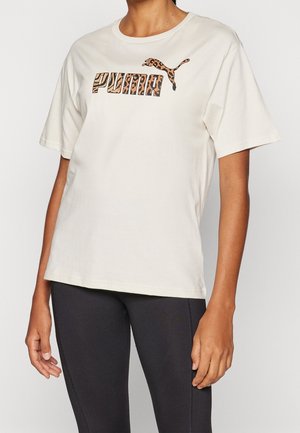 Person trägt ein weißes Puma-T-Shirt mit Leopardenmuster-Logo, kombiniert mit schwarzen enganliegenden Leggings vor einem einfarbigen Hintergrund.