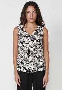 Blusa senza maniche in tessuto crema con una stampa floreale nera. Caratterizzata da una scollatura a V, chiusura con bottoni e dettaglio in vita arricciato.