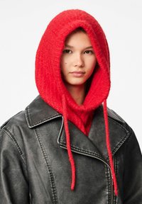 Capucha roja de punto unida a una chaqueta de cuero negra. La capucha tiene una textura con fibras visibles y cuenta con cuerdas largas.