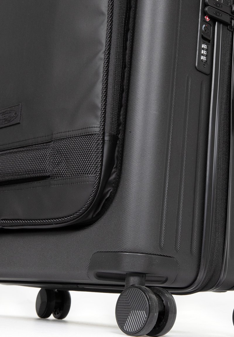 Valise rigide noire avec surface texturée, fermeture éclair et cadenas à combinaison, équipée de roues à roulement fluide et d'une poignée latérale.
