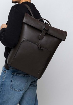 Brown leather backpack with a roll-top design, featuring a front zip pocket and leather strap closure. Smooth texture and minimal hardware.