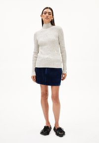 Lichtgrijze geribde turtlenecktrui met lange mouwen, gecombineerd met een donkerblauwe corduroy minirok. Zwarte schoenen met franjes.
