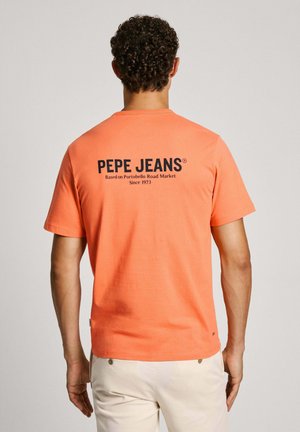 Narančasta pamučna majica s kratkim rukavima. Na leđima se nalazi crni tekst s brendom: "PEPE JEANS Temeljeno na Portobello Road Market od 1973."
