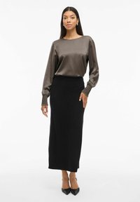 Brun satin bluse med lange ærmer og samlede manchetter, parret med en sort tætsiddende maxi-nederdel. Sorte spidse hæle fuldender looket.